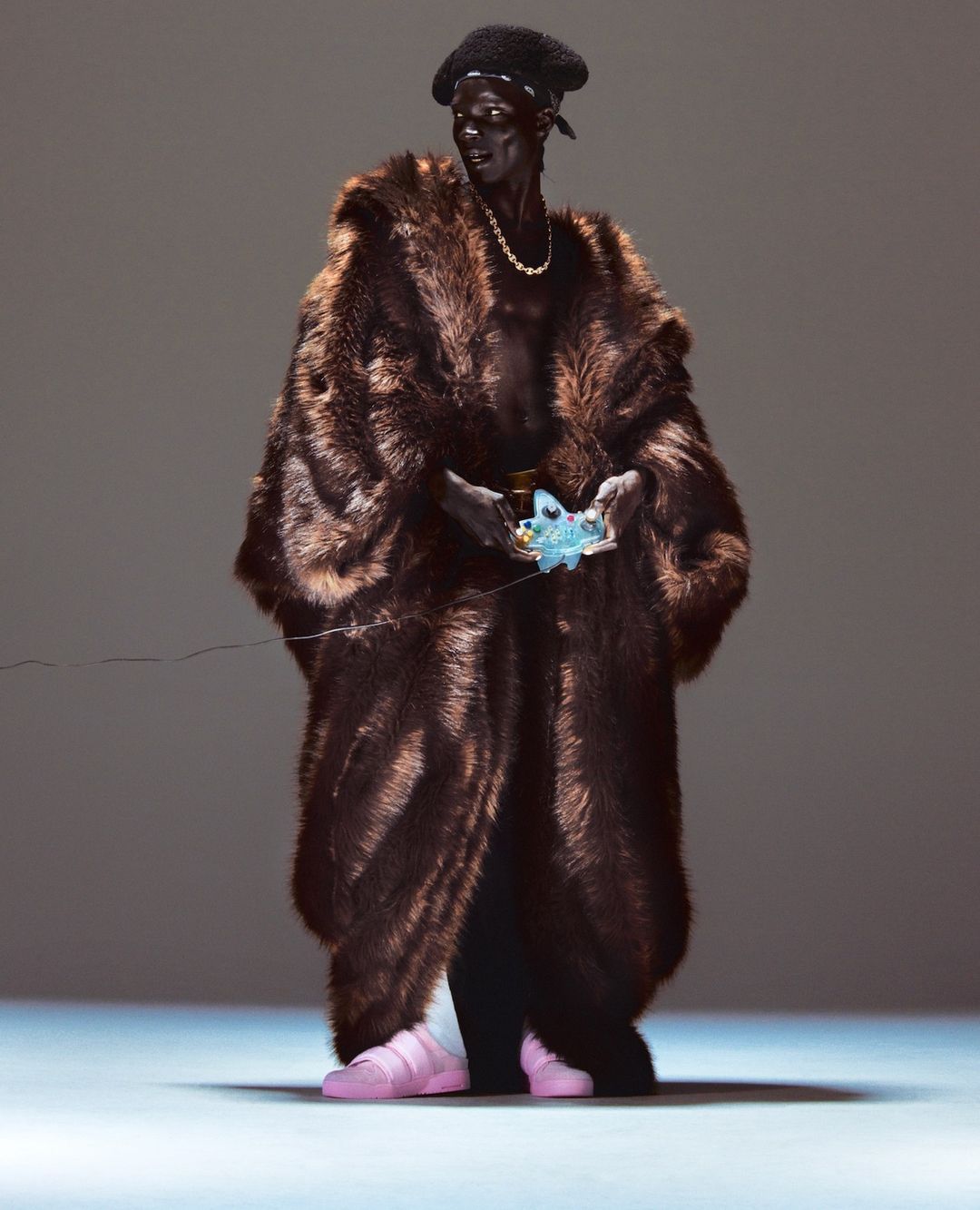 Full shot of a person in a brown fur coat, black pants, pink sneakers, and a black beret, holding an object in their hands.