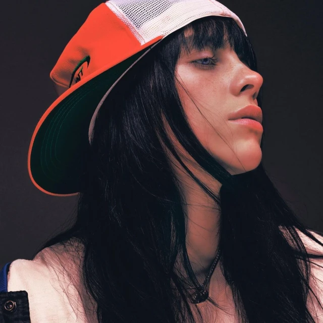 Close-up portrait of a fair-skinned woman with dark hair wearing a baseball cap, looking to the side in a photo studio setting.