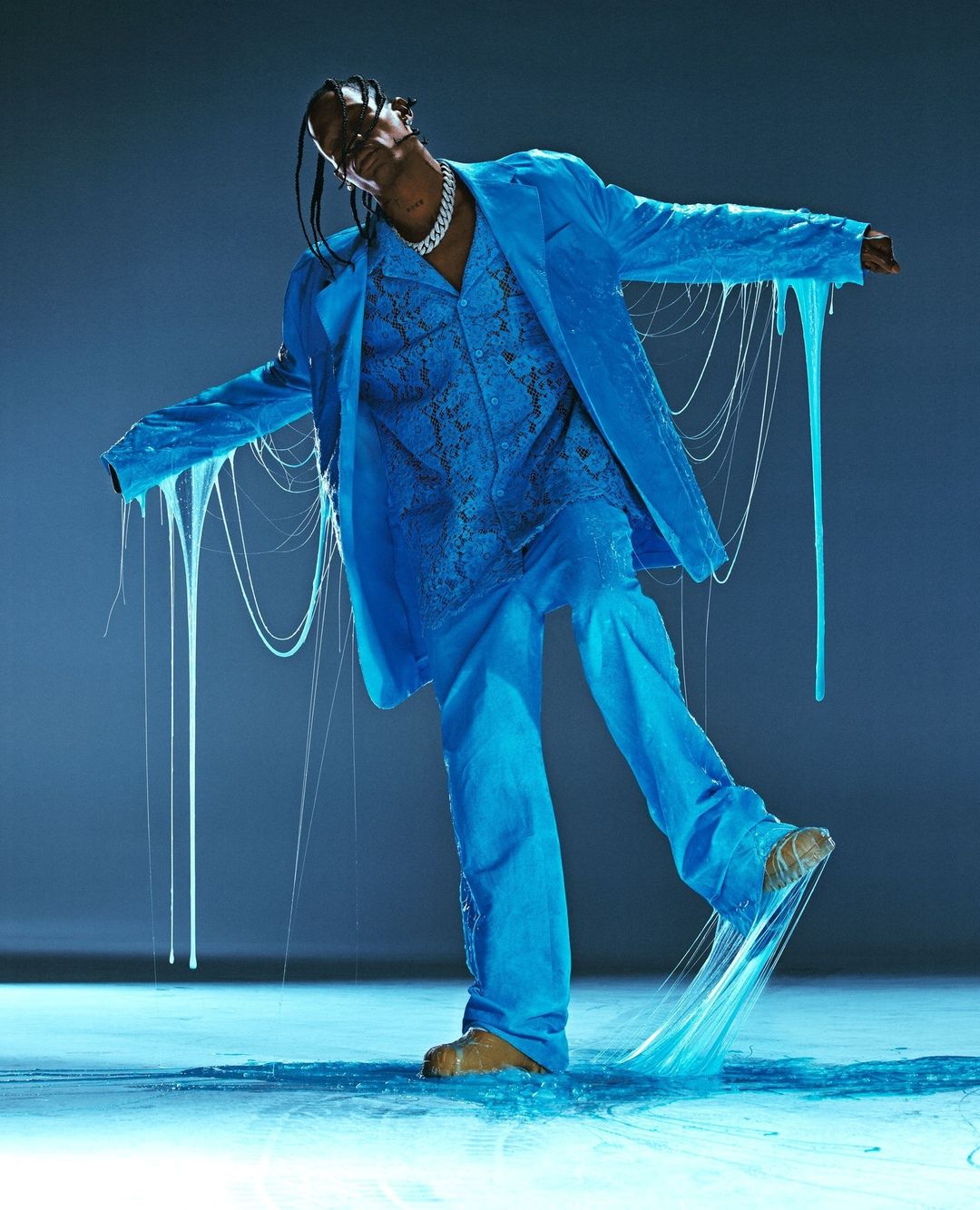 A man in a blue suit with slime dripping off it poses in a photo studio with dramatic lighting, showcasing a bold fashion choice.