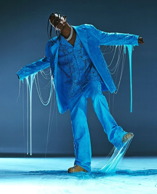 A man in a blue suit with slime dripping off it poses in a photo studio with dramatic lighting, showcasing a bold fashion choice.