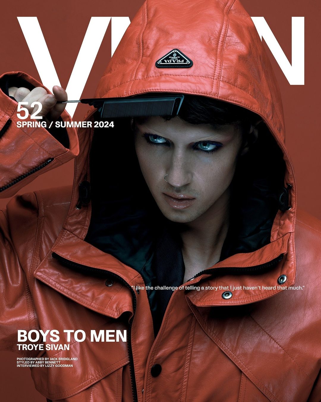 Magazine cover featuring a person with light skin and blue eyes wearing a red hooded jacket and black comb in their hair. Prada logo visible.