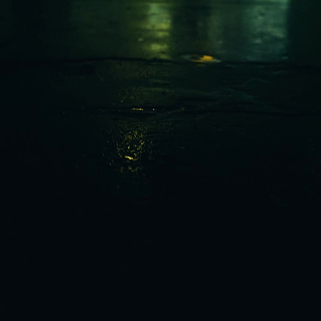 Abstract, dark image featuring the soft glow of streetlights reflecting on a wet surface, creating a moody urban scene at night.