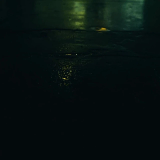Abstract, dark image featuring the soft glow of streetlights reflecting on a wet surface, creating a moody urban scene at night.