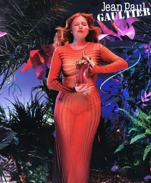 Adult female posing in a sheer orange dress, holding a perfume bottle in a lush botanical setting, with Jean Paul Gaultier text overlay.