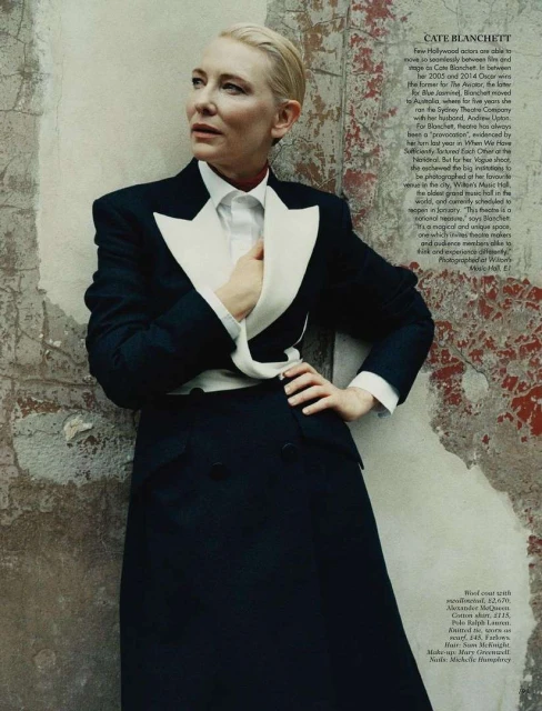 Elegant portrait of Cate Blanchett in a stylish black tuxedo suit with a white shirt against a distressed, textured wall backdrop.
