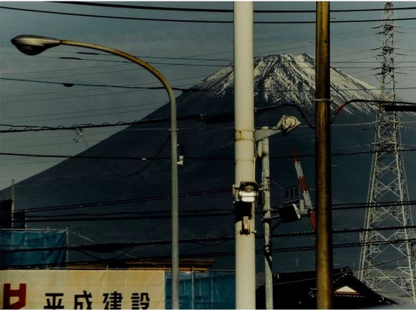 Cityscape featuring Mount Fuji in the background, streetlights, and utility poles with wires crisscrossing the sky in an urban scene.