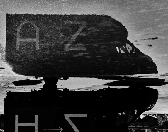 Black and white reflection photograph of an airplane, with the letters A and Z and a directional arrow visible on the plane.