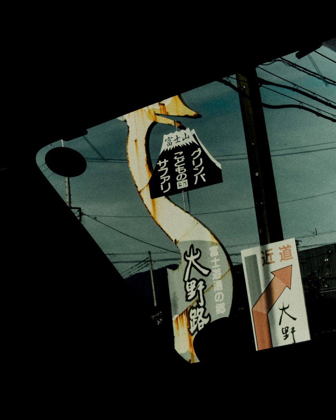 Vintage photograph showcases weathered Japanese signage along a roadside, reflecting a sense of travel and cultural exploration.