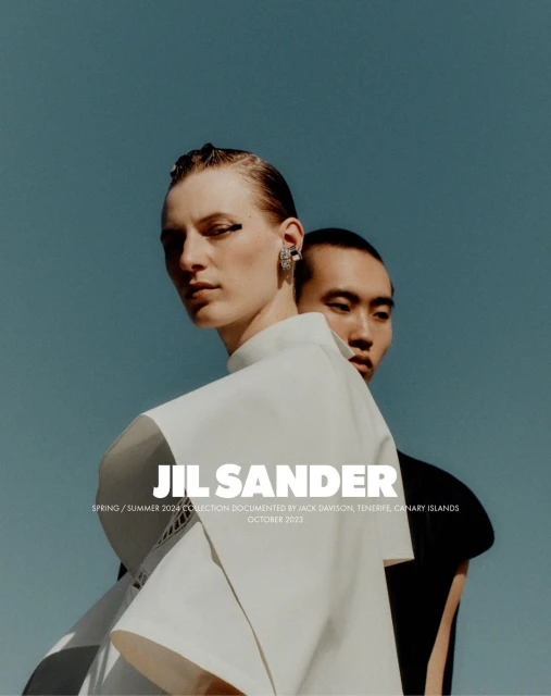 Fashion shot of two models, one fair-skinned wearing white and the other Asian, set against a blue sky. The focus is on stylish clothing.