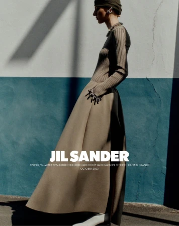 Fashion editorial photo featuring a woman wearing a long brown dress with statement bracelet accessories, posing against a blue and white wall.