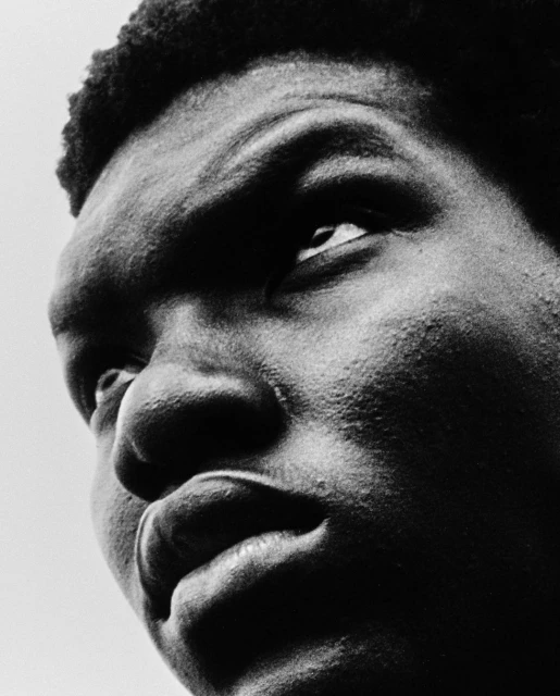 Close-up black and white portrait of a Black man looking up with his mouth slightly open, showcasing his face, hair, and skin texture.