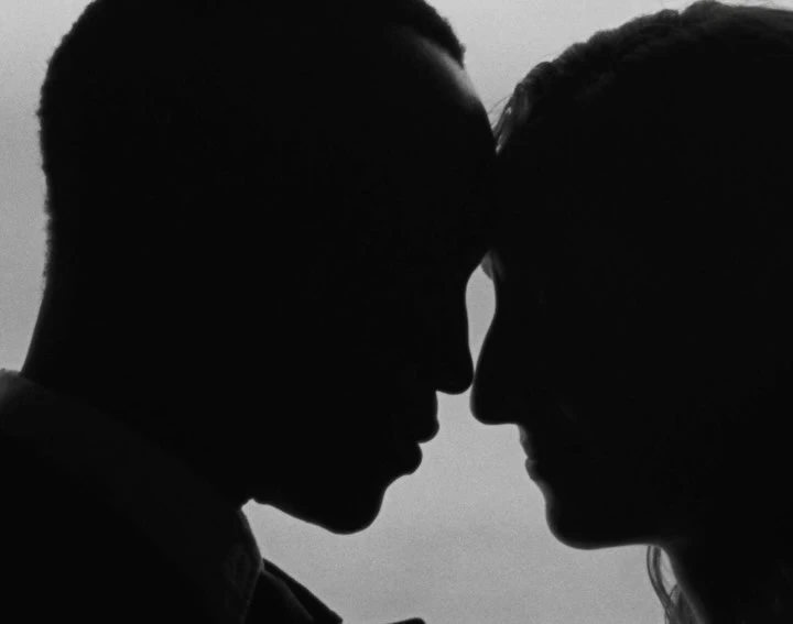 Black and white silhouette of an African American man and a Caucasian woman facing each other, close up, intimate moment.