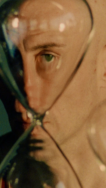 Close-up studio shot of adult male's face partially visible through glass, featuring an eye-level angle and warm color grading.