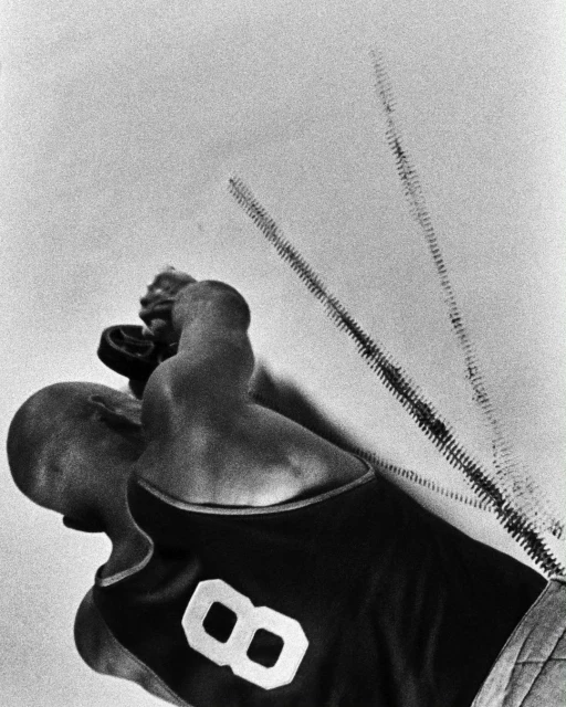Low-angle shot of bald adult male wearing a sports jersey with the number 8, holding a basketball with motion trails in black and white.