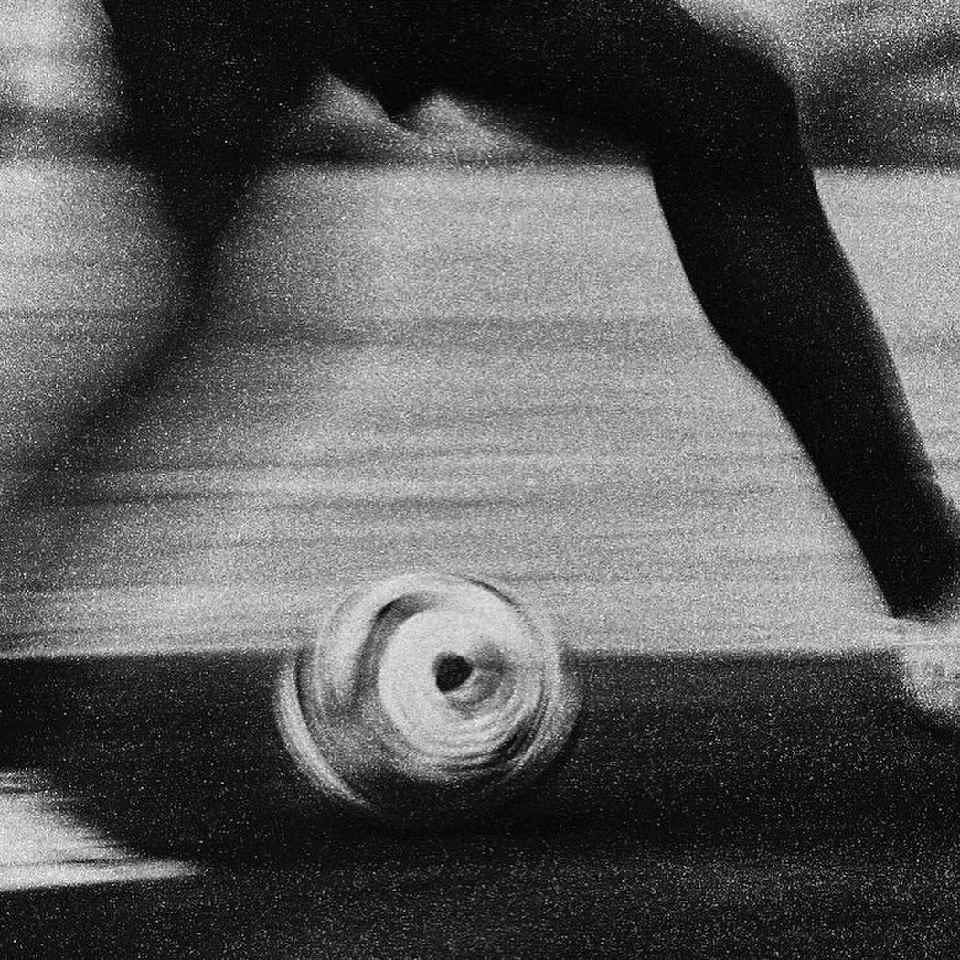 Black and white photo of a soccer ball in motion on a field, with a person's leg and foot visible in the background.
