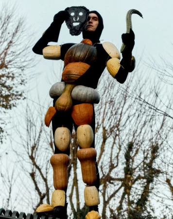 A person wearing an unusual pumpkin costume with a mask, standing outdoors with bare trees in the background, creating a unique, odd image.