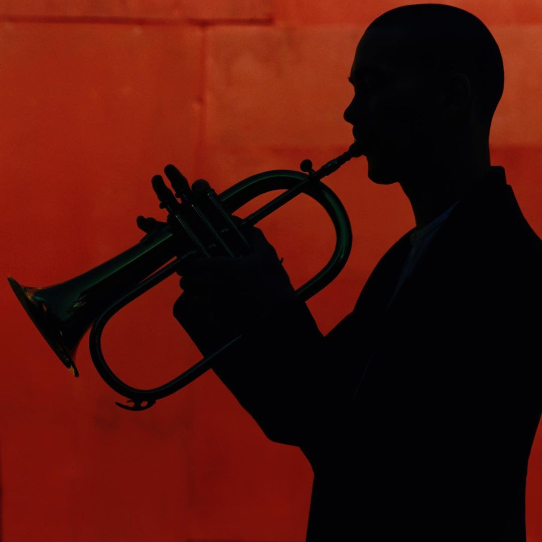 Silhouette of a man playing a flugelhorn against an orange background, showcasing musical performance and artistic silhouette photography.