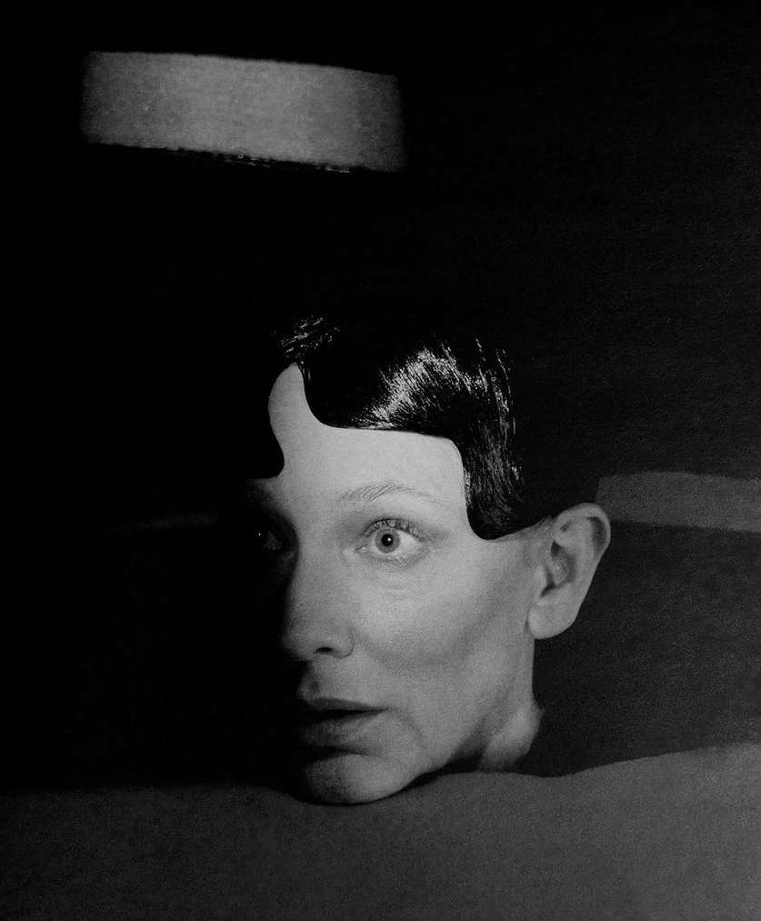 Monochrome portrait of a woman with short dark hair, looking up with a surprised expression, in a dark, minimalist environment.