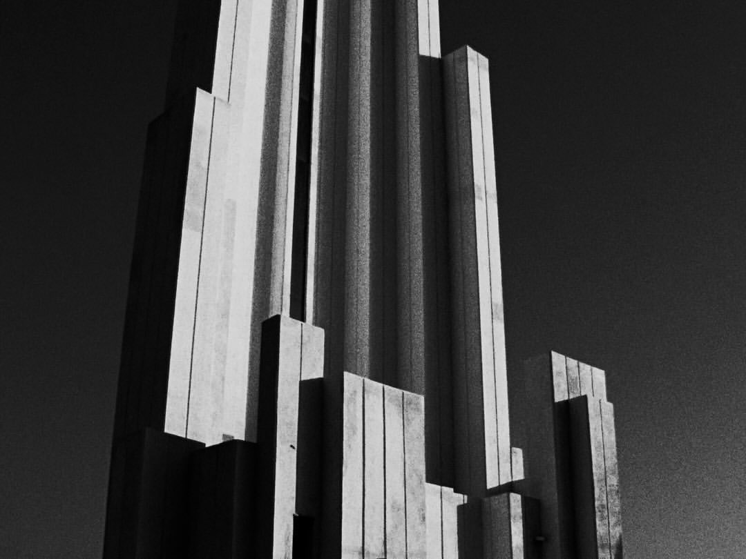 Black and white photograph of a modern architectural structure featuring strong vertical lines and varying heights under a dark sky.
