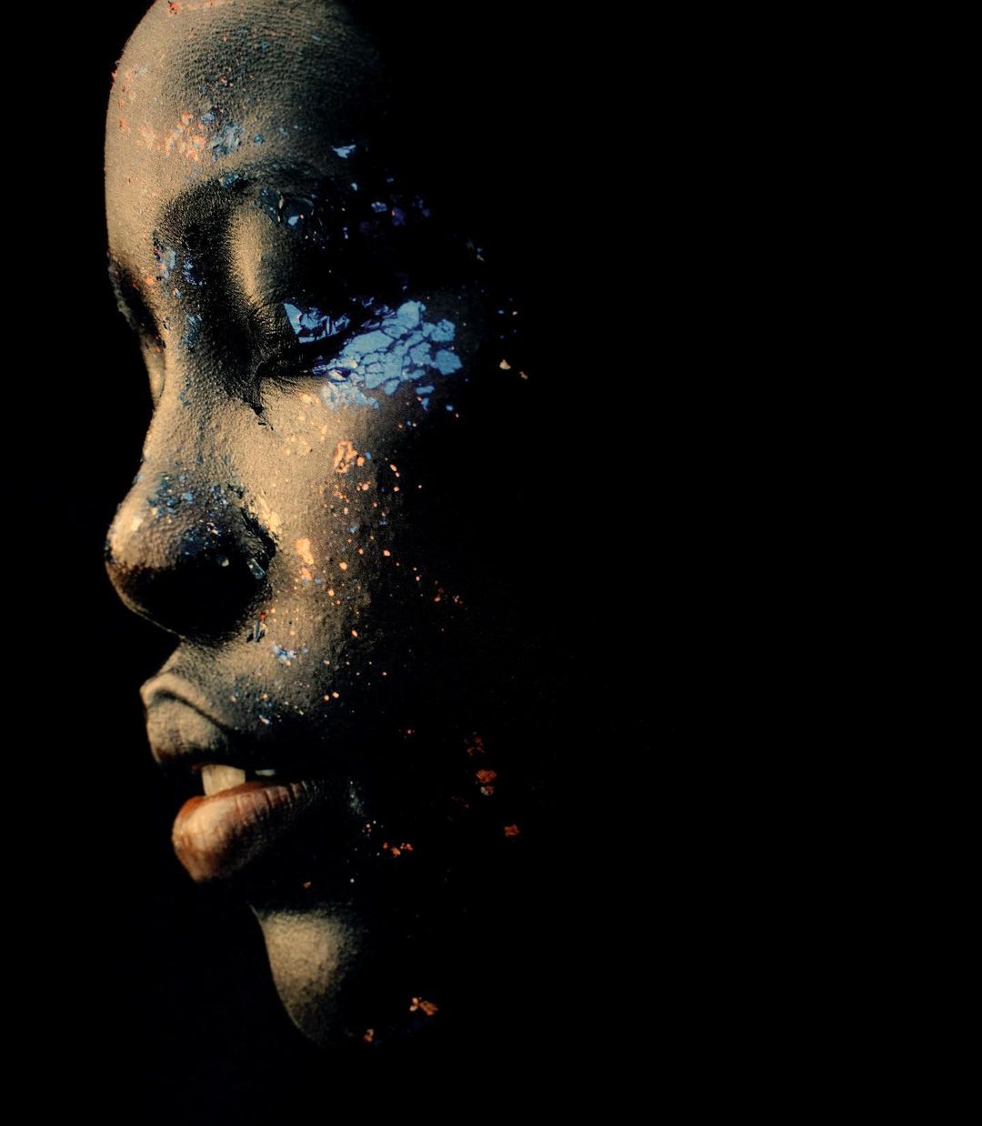 Profile of a face with textured skin and glitter on a black background in a portrait with selective focus and low-key lighting.