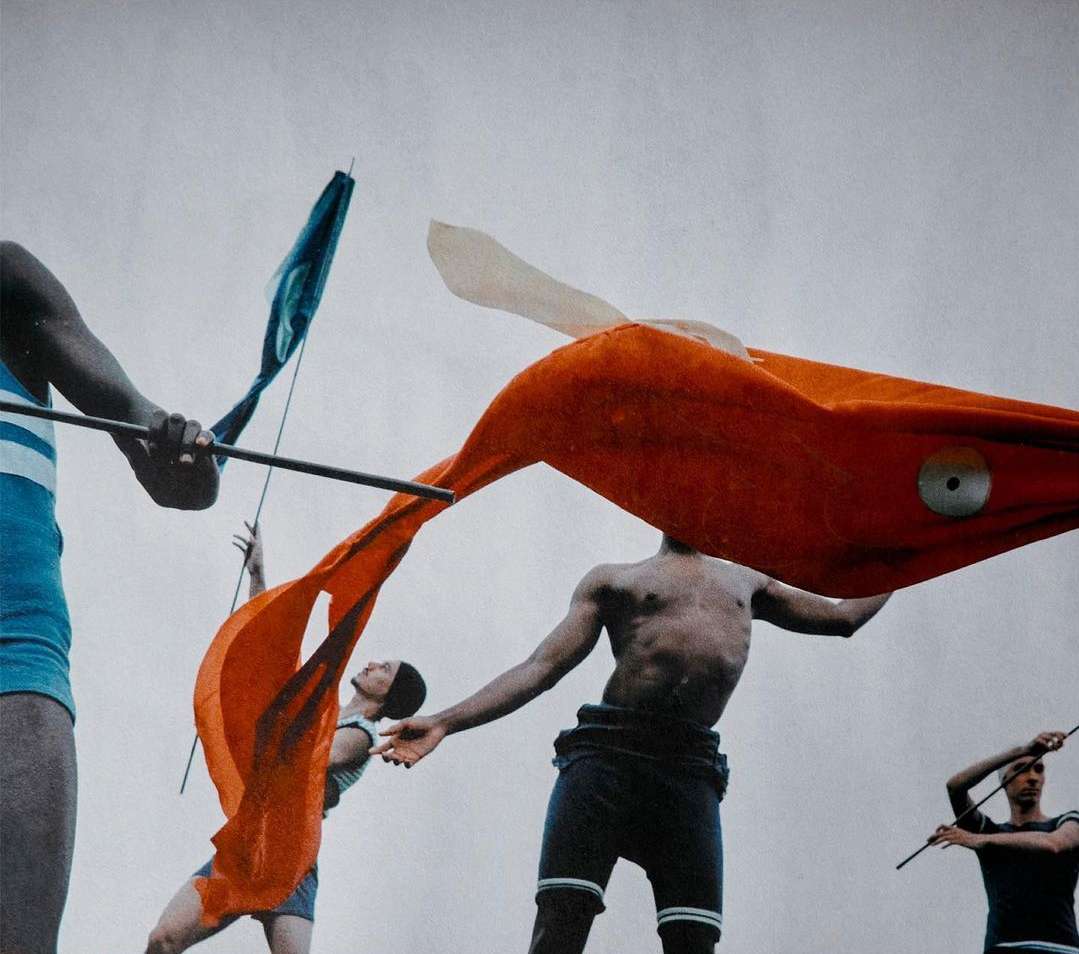 Multiple people holding and wearing orange, blue, and white flags. The flags are in motion against a white background. Clothing is striped.