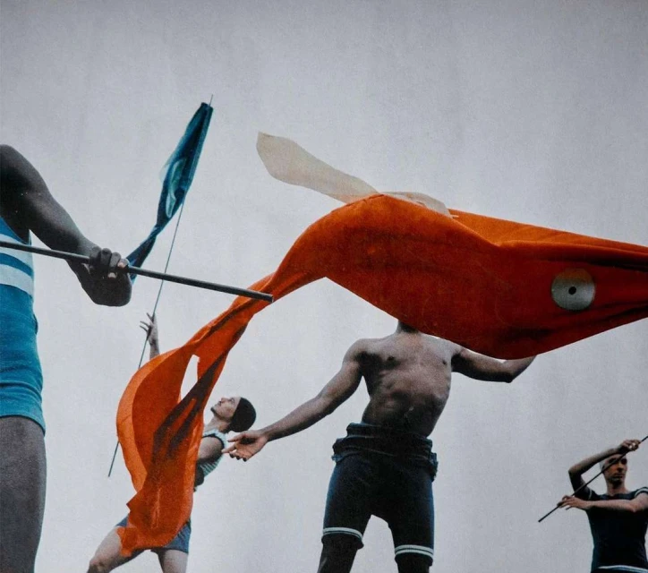 Multiple people holding and wearing orange, blue, and white flags. The flags are in motion against a white background. Clothing is striped.
