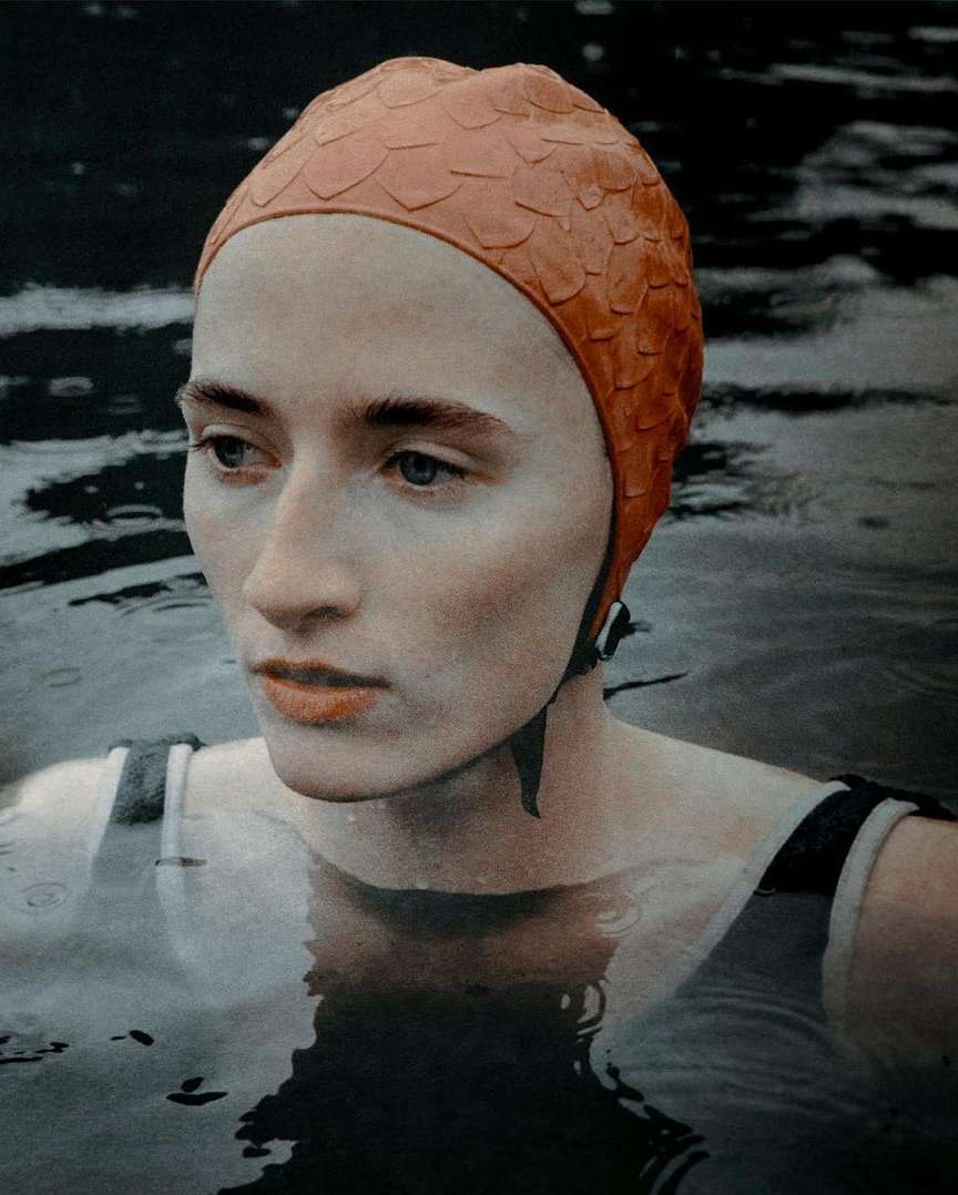 Woman with vintage swim cap in water. Portrait of a swimmer with fair skin wearing a textured orange bathing cap at the lake.