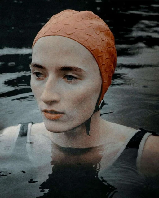 Woman with vintage swim cap in water. Portrait of a swimmer with fair skin wearing a textured orange bathing cap at the lake.