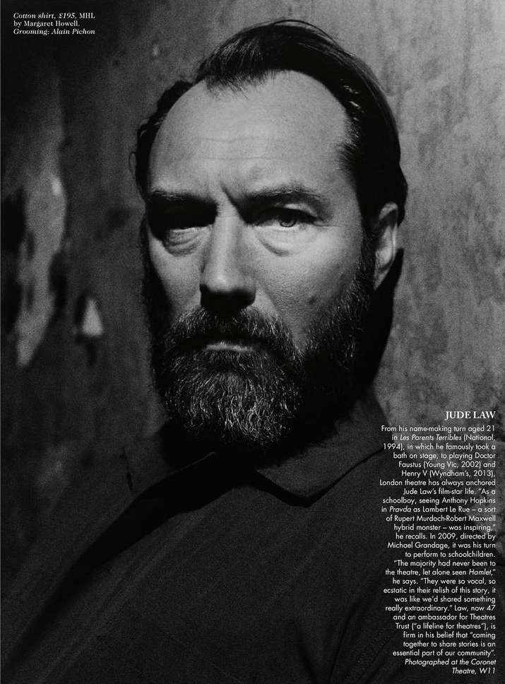 Monochrome portrait of Jude Law with a beard, gazing intensely into the camera against a textured wall backdrop, captured in a medium shot.