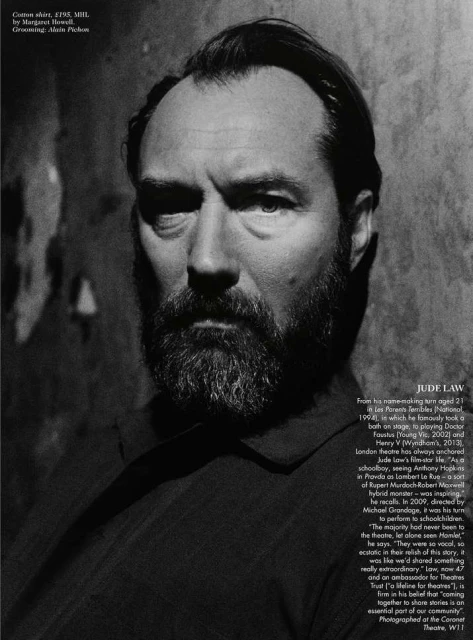 Monochrome portrait of Jude Law with a beard, gazing intensely into the camera against a textured wall backdrop, captured in a medium shot.
