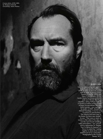 Monochrome portrait of Jude Law with a beard, gazing intensely into the camera against a textured wall backdrop, captured in a medium shot.