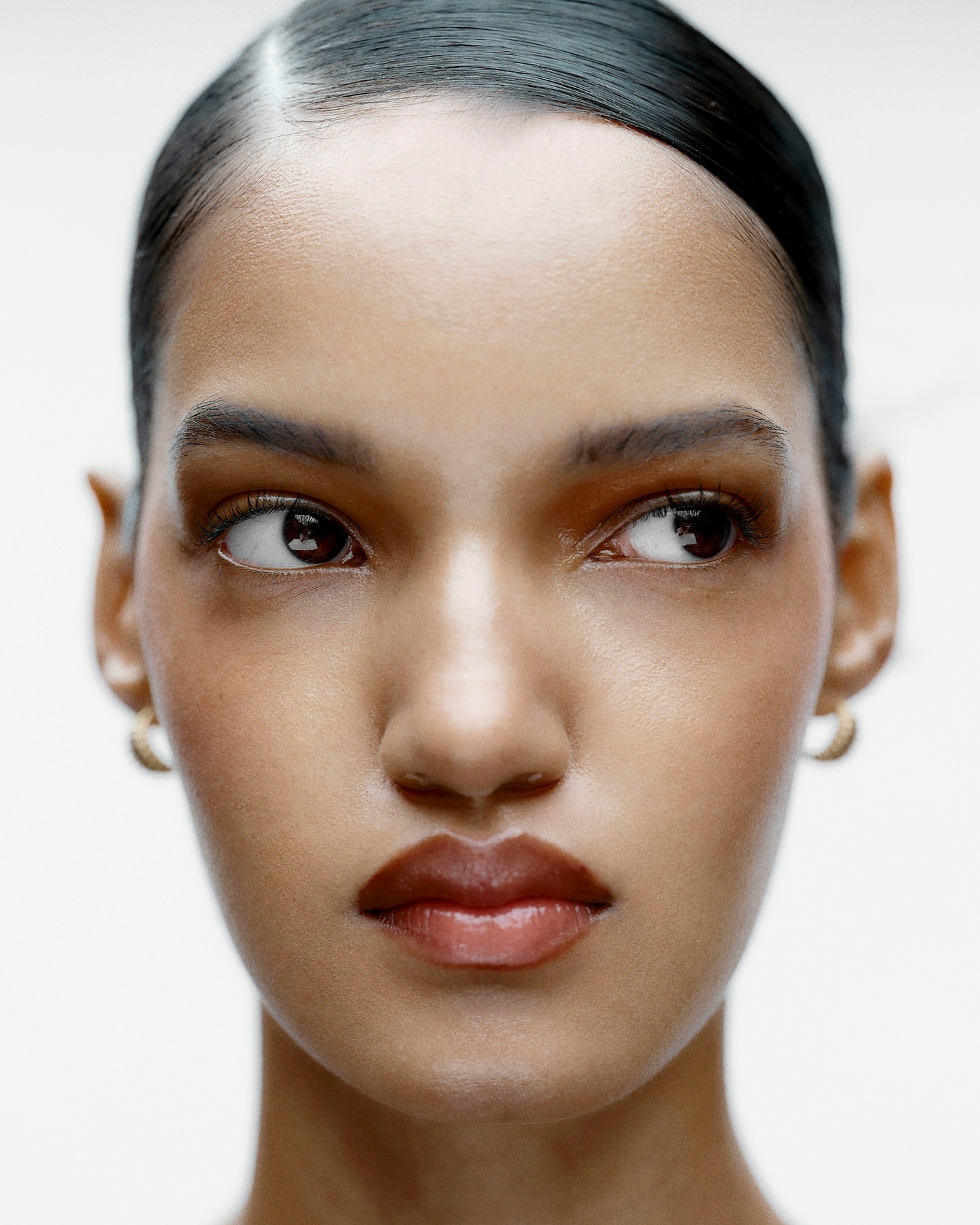 Close-up portrait of an adult female with brown hair and skin looking off to the side against a white background in a beauty shot.