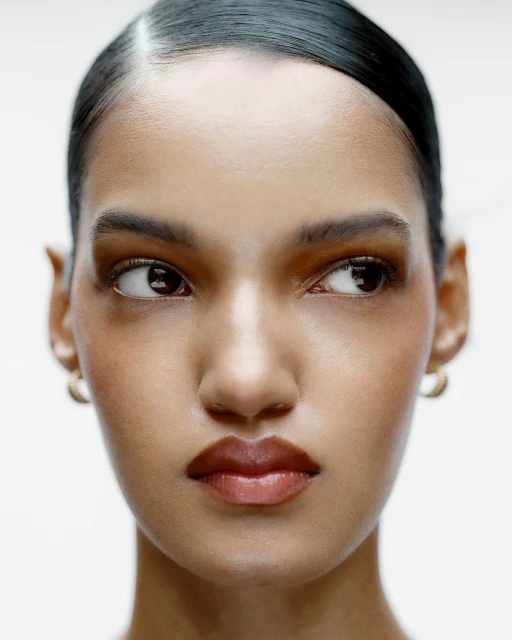 Close-up portrait of an adult female with brown hair and skin looking off to the side against a white background in a beauty shot.