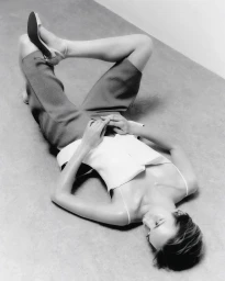Model lying on the floor with knees up and heels in the air wearing tailored shorts and a camisole in a black and white photograph