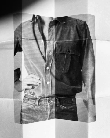 Monochromatic image of model wearing a collared shirt, jeans, hand on hip, presented on folded paper; evokes a vintage editorial style.