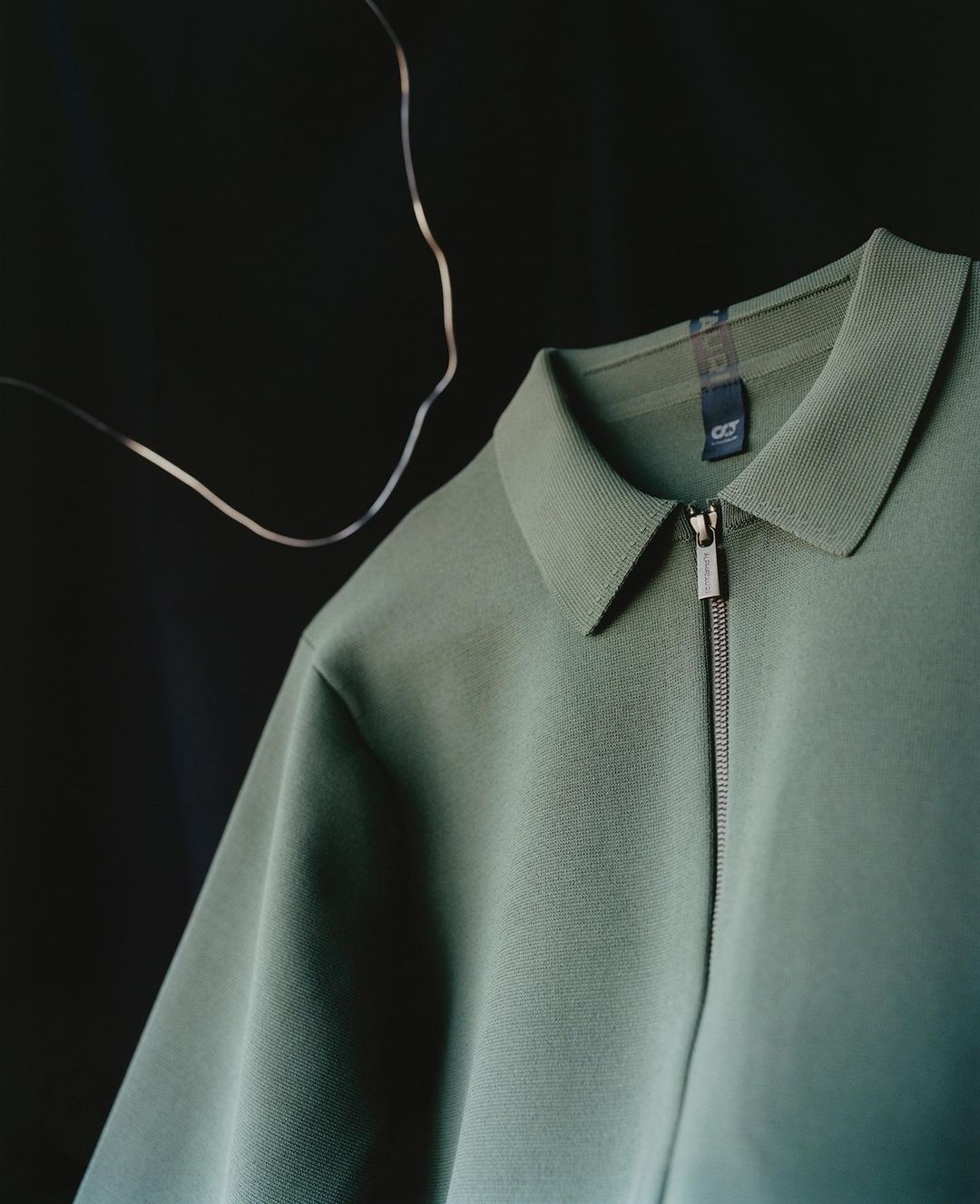 Studio shot of a green polo shirt with a zipper on a dark background, showcasing its color and design with soft lighting.