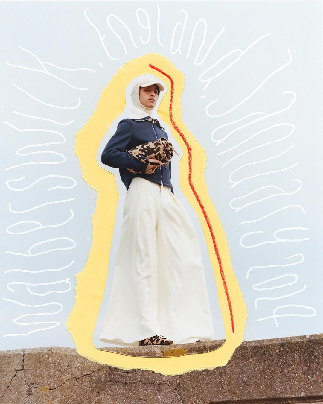 Fashion shot of a person wearing a white head covering, navy jacket, wide white trousers and carrying a leopard print bag, outdoors.