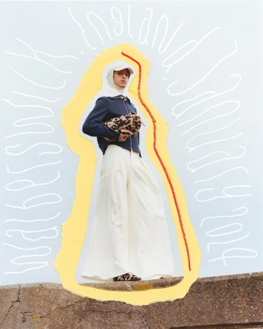 Fashion shot of a person wearing a white head covering, navy jacket, wide white trousers and carrying a leopard print bag, outdoors.