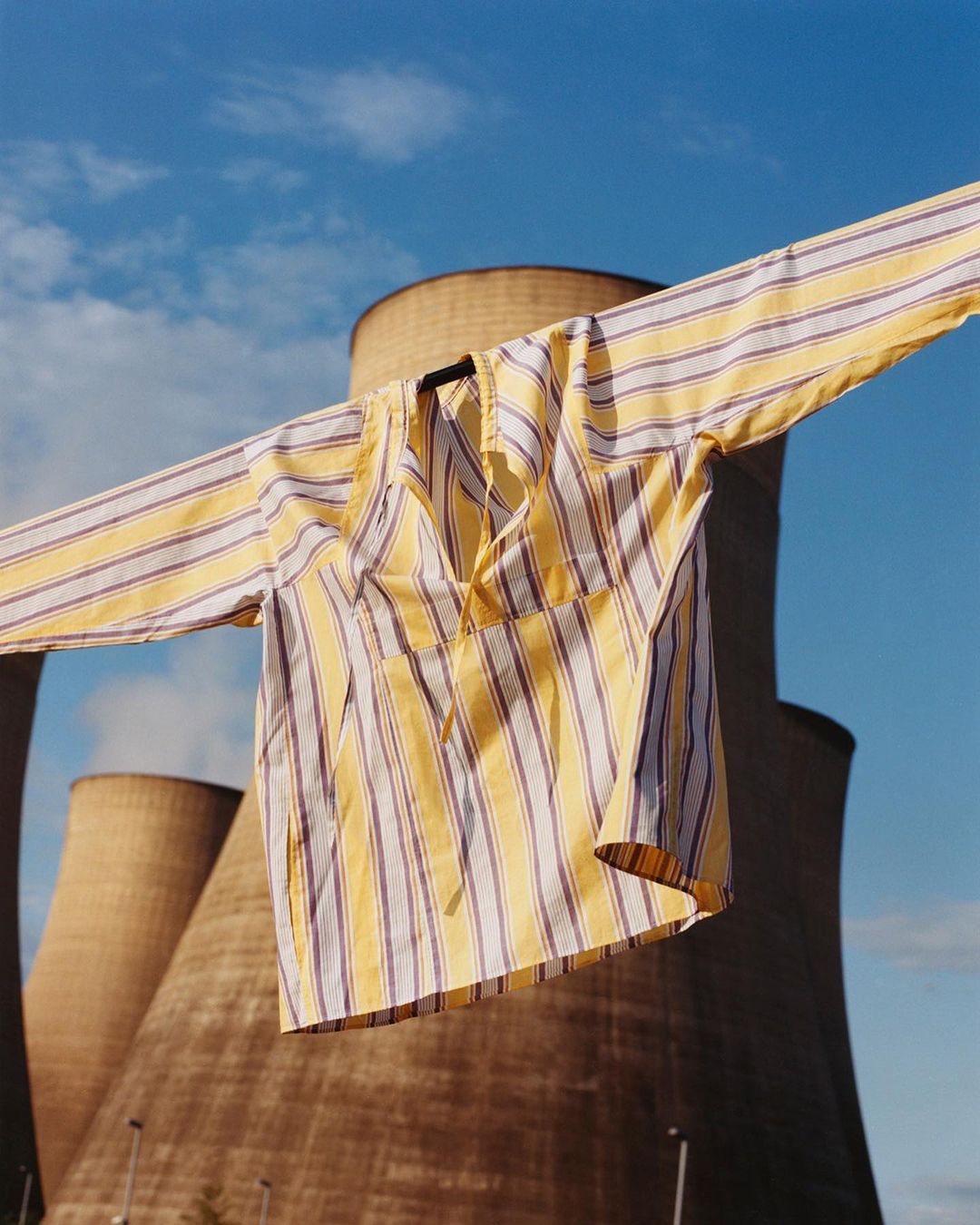 Striped shirt on a hanger, photographed against a background of power plant cooling towers and a blue sky with scattered clouds.