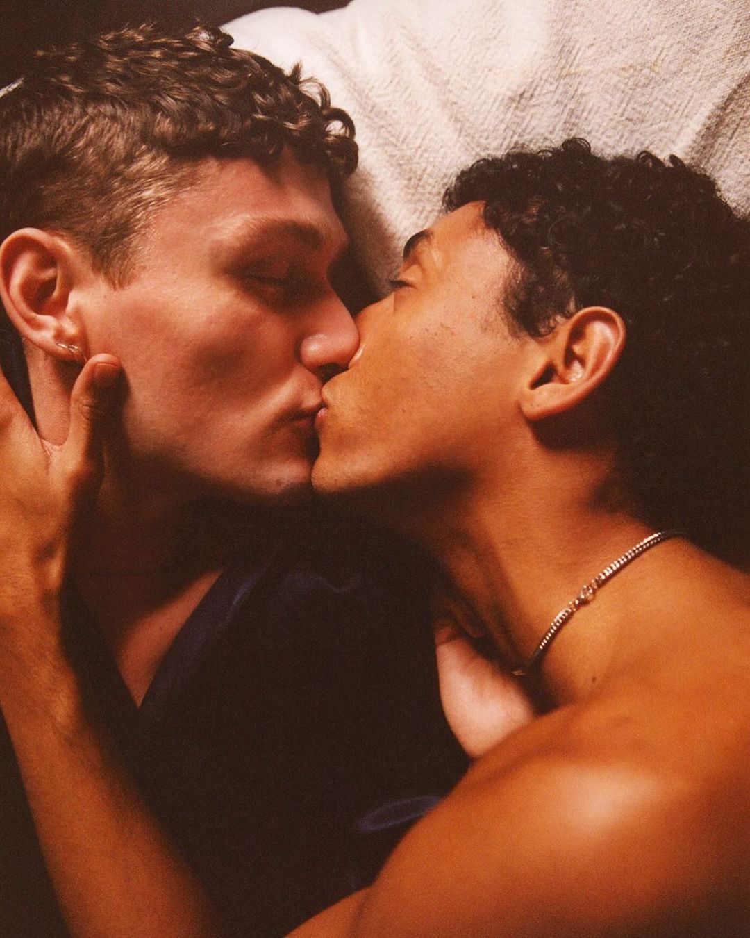 Close-up shot of two adult men embracing and kissing tenderly, showcasing their faces and features, set against a neutral background.