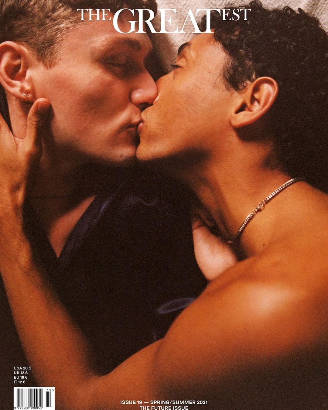 Two adult males embrace and kiss on magazine cover. The dark-haired man wears a silver chain necklace. Text overlay includes magazine name.