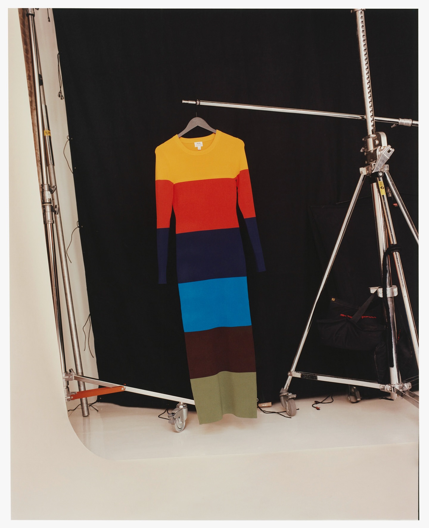 Colorful striped knit dress on a hanger in a photo studio setting with lighting equipment and a black backdrop providing contrast.