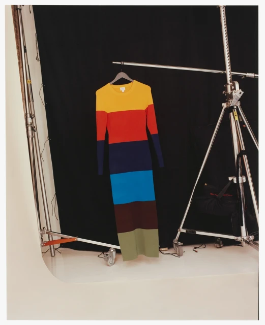 Colorful striped knit dress on a hanger in a photo studio setting with lighting equipment and a black backdrop providing contrast.