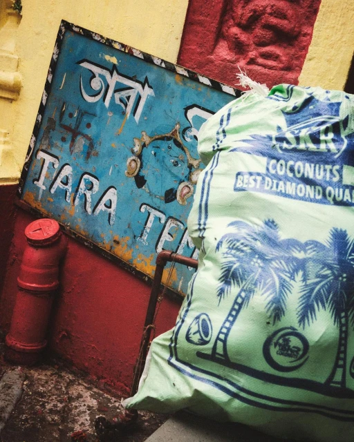 Vintage blue and yellow sign with red canister and a sack printed with palm trees leaning against a wall.