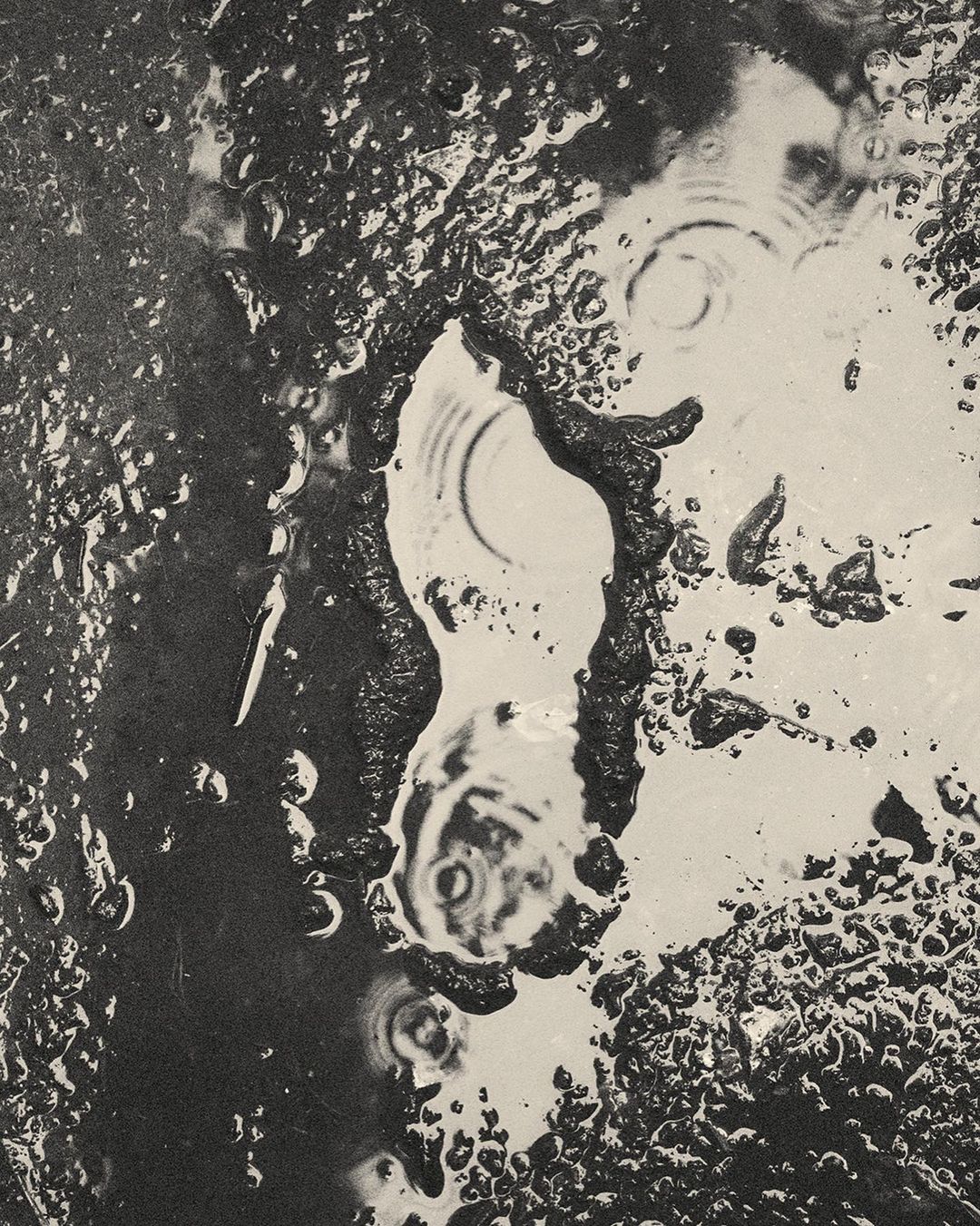 Abstract black and white photograph of water puddles and ripples on a dark surface, creating a unique artistic composition.