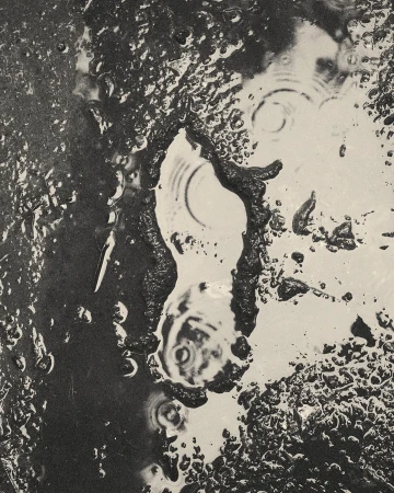 Abstract black and white photograph of water puddles and ripples on a dark surface, creating a unique artistic composition.