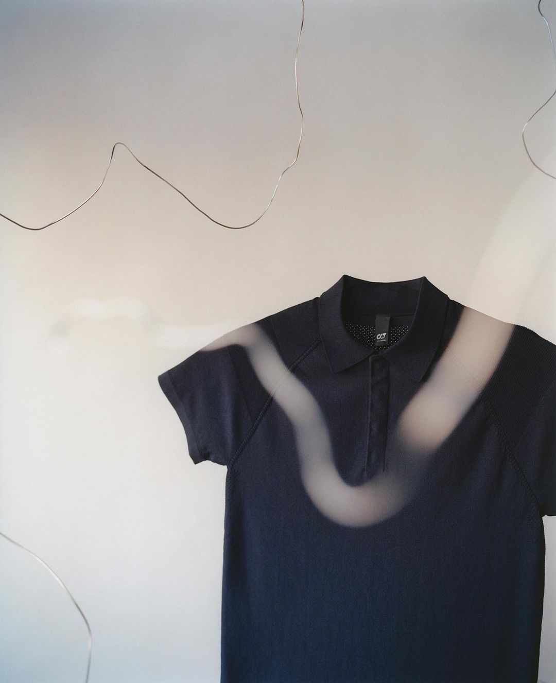 A dark blue polo shirt is set against a light backdrop and illuminated by an abstract light pattern, creating a studio shot.