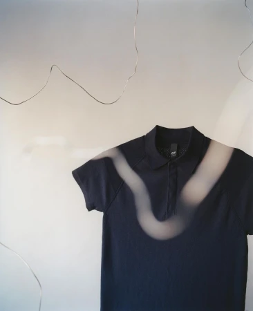 A dark blue polo shirt is set against a light backdrop and illuminated by an abstract light pattern, creating a studio shot.