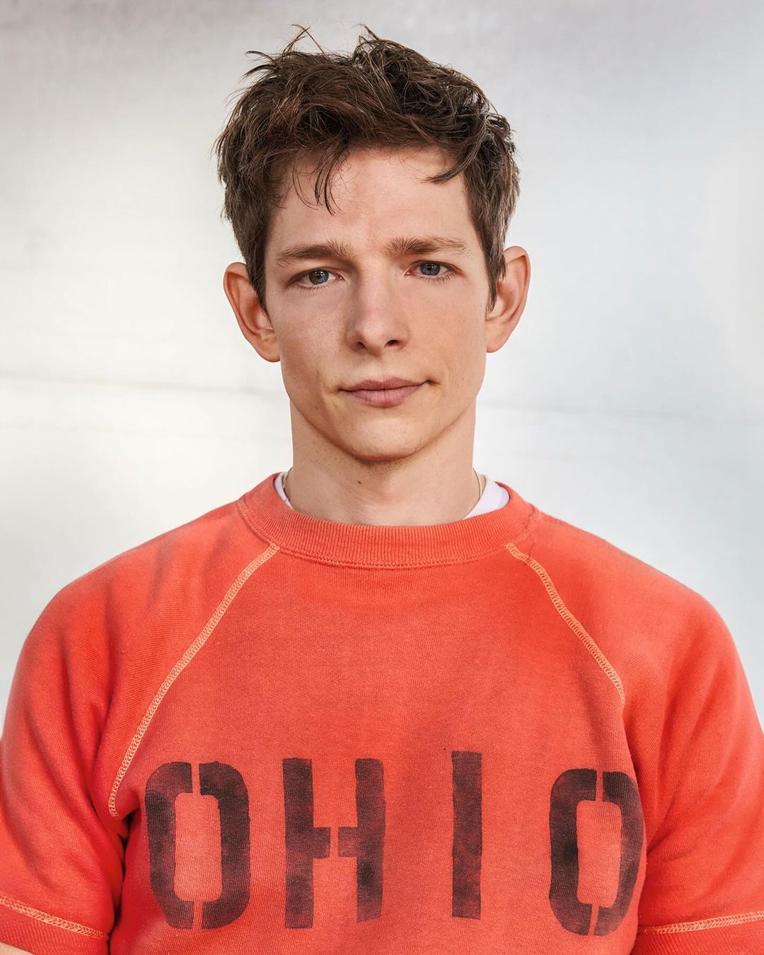 Portrait of an adult male with short brown hair, wearing an orange t-shirt with 'OHIO' printed in black letters, in a studio setting.