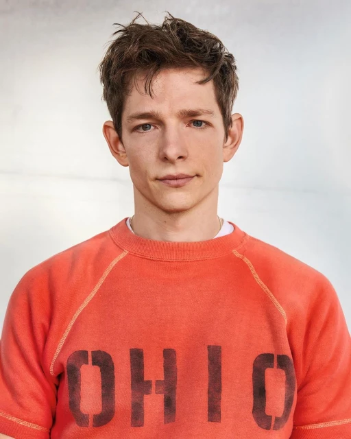 Portrait of an adult male with short brown hair, wearing an orange t-shirt with 'OHIO' printed in black letters, in a studio setting.